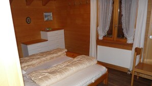 Een slaapkamer met houten lambrisering, een tweepersoonsbed, een nachtkastje van hout, een dressoir en een raam met gordijnen.