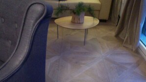 Um quarto com chão de azulejos estampados, uma mesa de centro redonda com uma planta e um sofá.