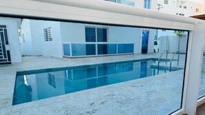 A swimming pool with a glass enclosure, a white exterior wall, and a blue door in the background. - sol y arena bayahibe (Bayahíbe)