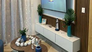 A modern living room with a flat-screen TV mounted on a wooden wall, a round coffee table with decorative items, and a ceiling fan. - sol y arena bayahibe (Bayahíbe)
