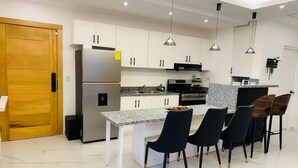 A modern kitchen with white cabinets, a granite countertop, a stainless steel refrigerator, and black chairs with gold legs. - sol y arena bayahibe (Bayahíbe)