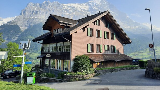 A traditional chalet with a sloped roof, large windows, and a view of snow-capped mountains in the background. - Eschengasse 21 by Interhome (Grindelwald)