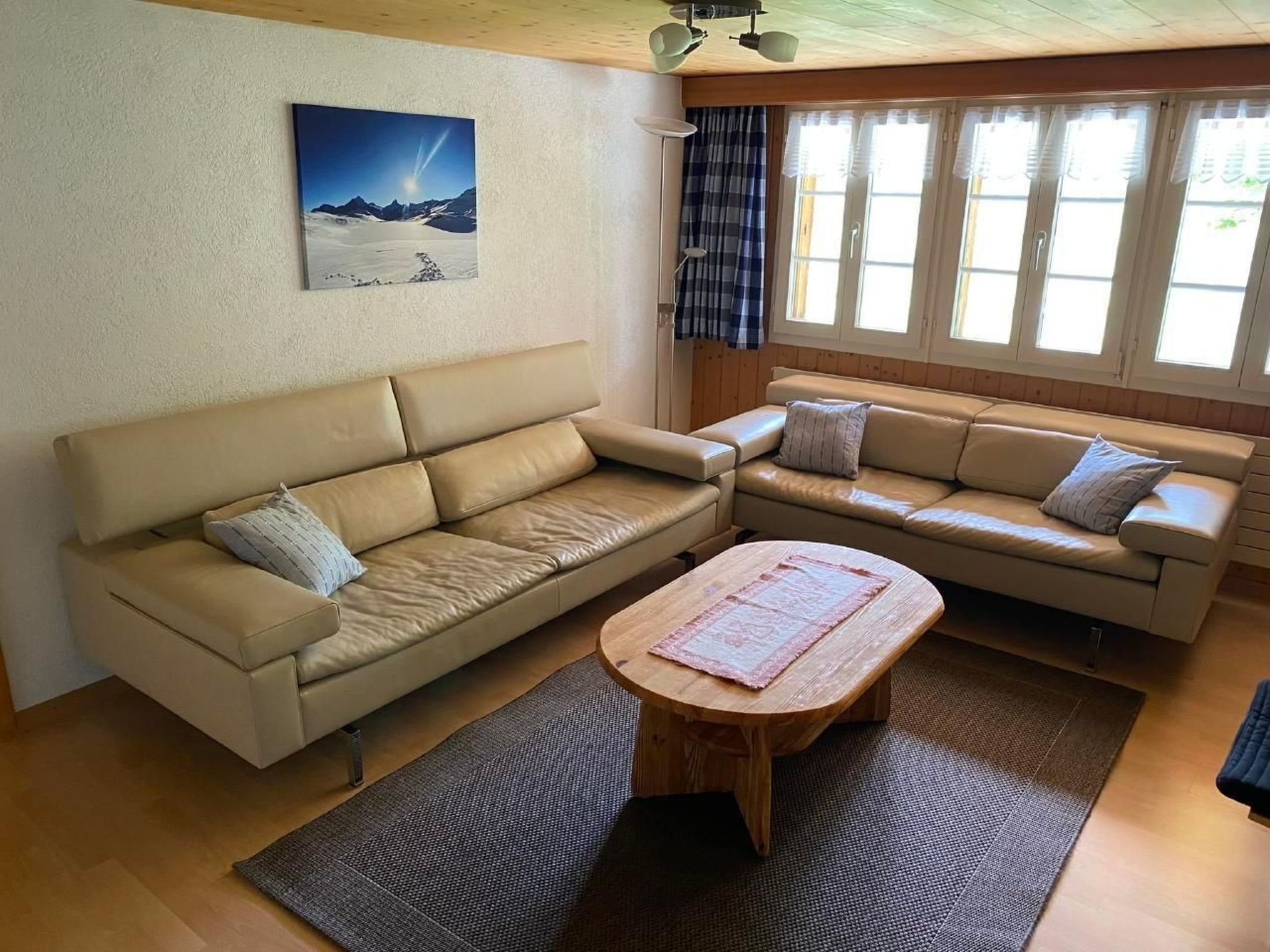 Ein Wohnzimmer mit zwei beigen Sofas, einem Holztisch und einem großen Fenster mit Vorhängen.