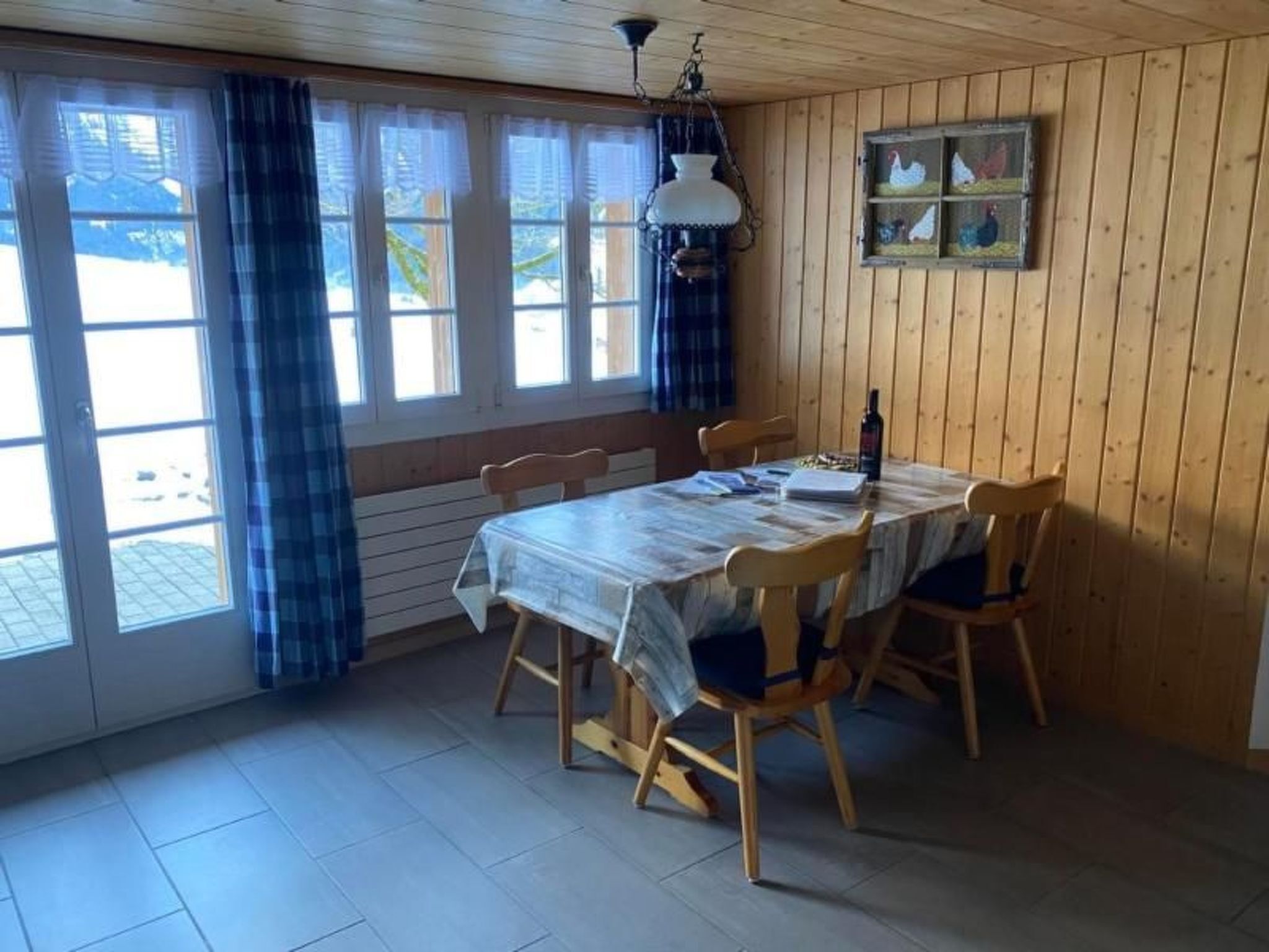 Ein Essbereich mit Holztisch und Stühlen, einer Hängelampe und einem Fenster mit Vorhängen.