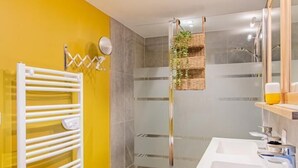 Ein modernes Badezimmer mit gelber Wand, einem weißen Heizkörper, einer Duschkabine aus Glas und einem weißen Waschbecken.