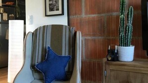 Ein modernes Wohnzimmer mit einem einzigartigen Sessel, einer Kakteenpflanze und gerahmten Bildern an der Wand.