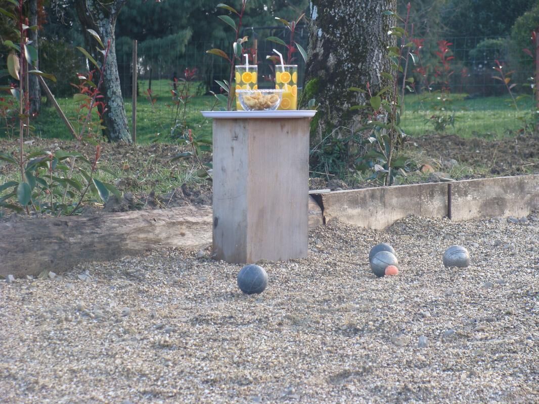 Estructura de madera con una mesa y dos vasos de zumo de naranja, rodeada de piedras y algunas pelotas deportivas.