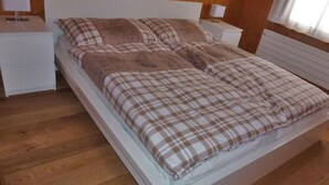 A bed with a plaid bedspread, two bedside tables with lamps, and wooden flooring. - Chalet Bachsbort 14 by Interhome (Grindelwald)
