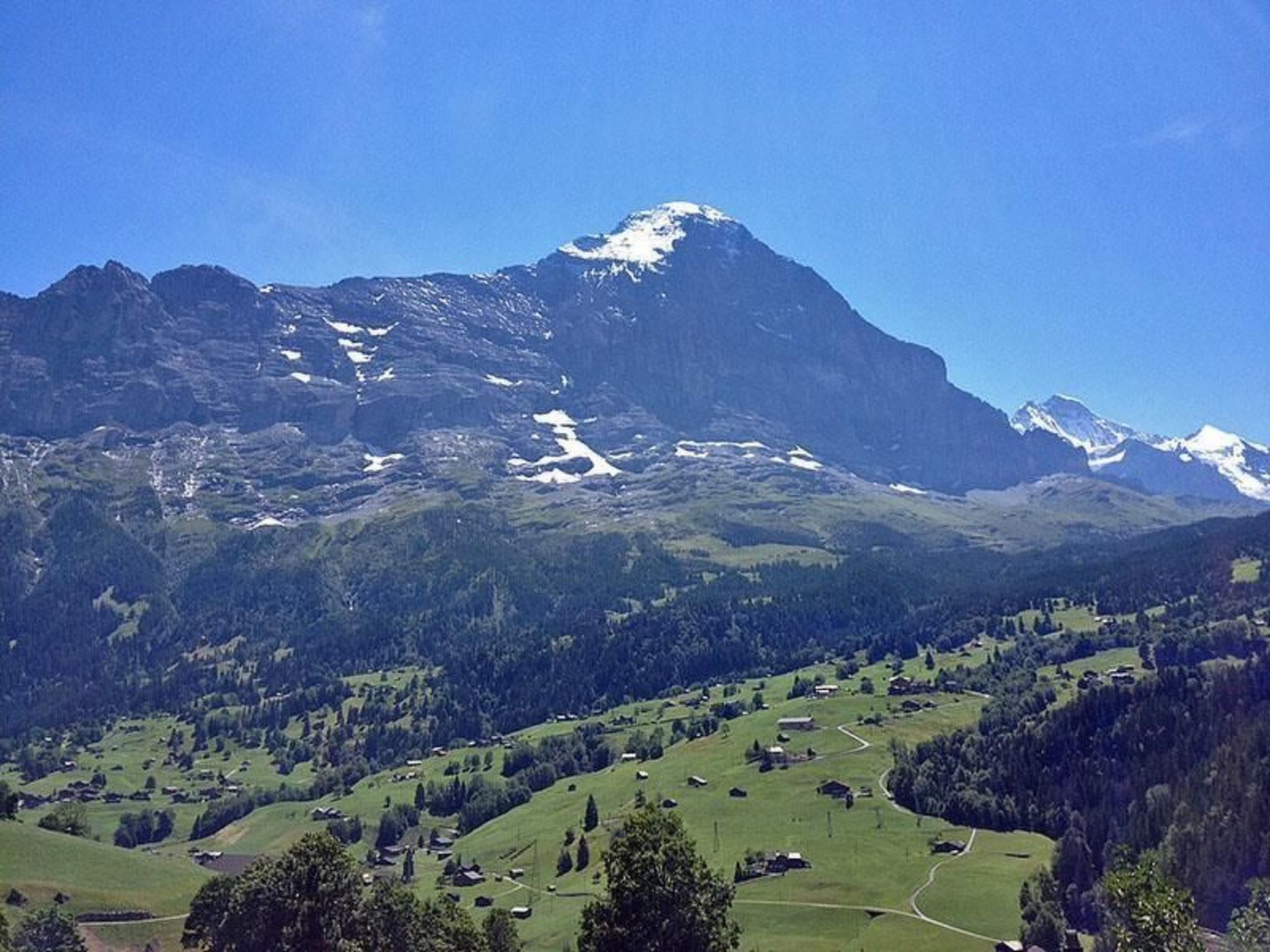 Eine gebirgige Landschaft mit einem markanten Gipfel, grünen Tälern und verstreuten Gebäuden.