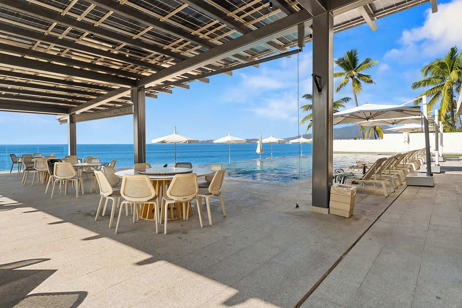 Un espace extérieur aménagé avec des tables et des chaises, offrant une vue sur une piscine et une plage.