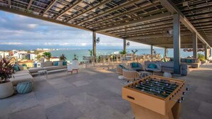 Un espace extérieur aménagé avec une table de baby-foot, des fauteuils confortables et une vue sur la mer.