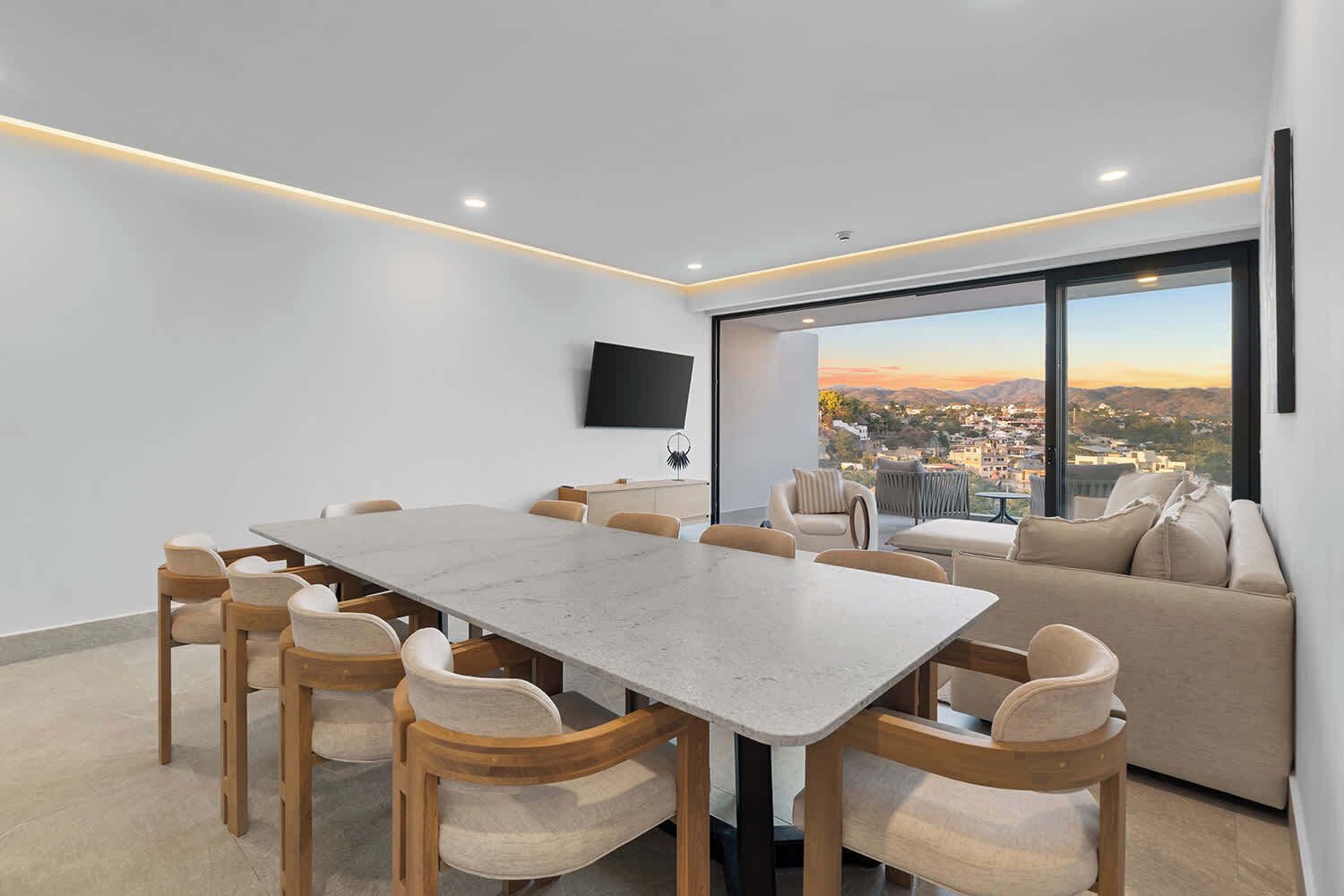 Een moderne eetruimte met een grote tafel en stoelen, een bank en een aan de muur bevestigde televisie.