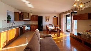 A modern kitchen with wooden cabinets, a dining area with a table and chairs, and a sofa in the foreground. - Apartment Katarina by Interhome (Krk/Milohnići)