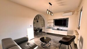Ein modernes Wohnzimmer mit einer Couch, einem Couchtisch und einem Fernseher im Hintergrund.