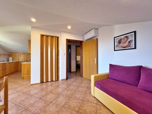 Ein Wohnzimmer mit einem violetten Sofa, Holzschränken und einer Küchenzeile mit einer Kaffeemaschine.
