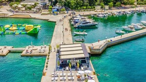 An aerial view of a marina with a docked boat, a swimming area, and a building with outdoor seating. - Jasnica by Interhome (Krk/Milohnići)
