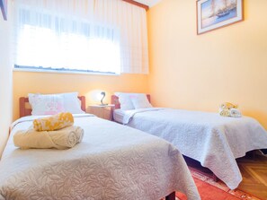 A hotel room with two beds, each with a white quilted bedspread and pillows. There is a small table with a lamp between the beds, and a painting on the wall. - Familienwohnung in Malinska by Interhome (Krk/Milohnići)