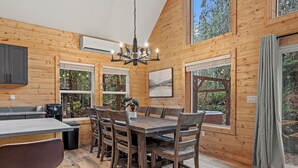 A wooden cabin interior with a dining table, chairs, a chandelier, and large windows. - 3-bedroom A-Frame w/ Hot Tub, Sauna, WiFi and EV charging (Ashford)