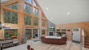 A spacious interior with a large dining area, a fireplace, and a view of the surrounding forest. - 3-bedroom A-Frame w/ Hot Tub, Sauna, WiFi and EV charging (Ashford)