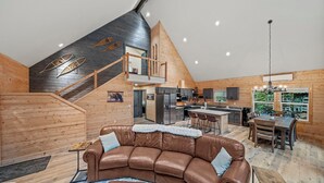 A spacious loft-style living area with a brown leather sofa, a dining table, and a kitchen in the background. - 3-bedroom A-Frame w/ Hot Tub, Sauna, WiFi and EV charging (Ashford)