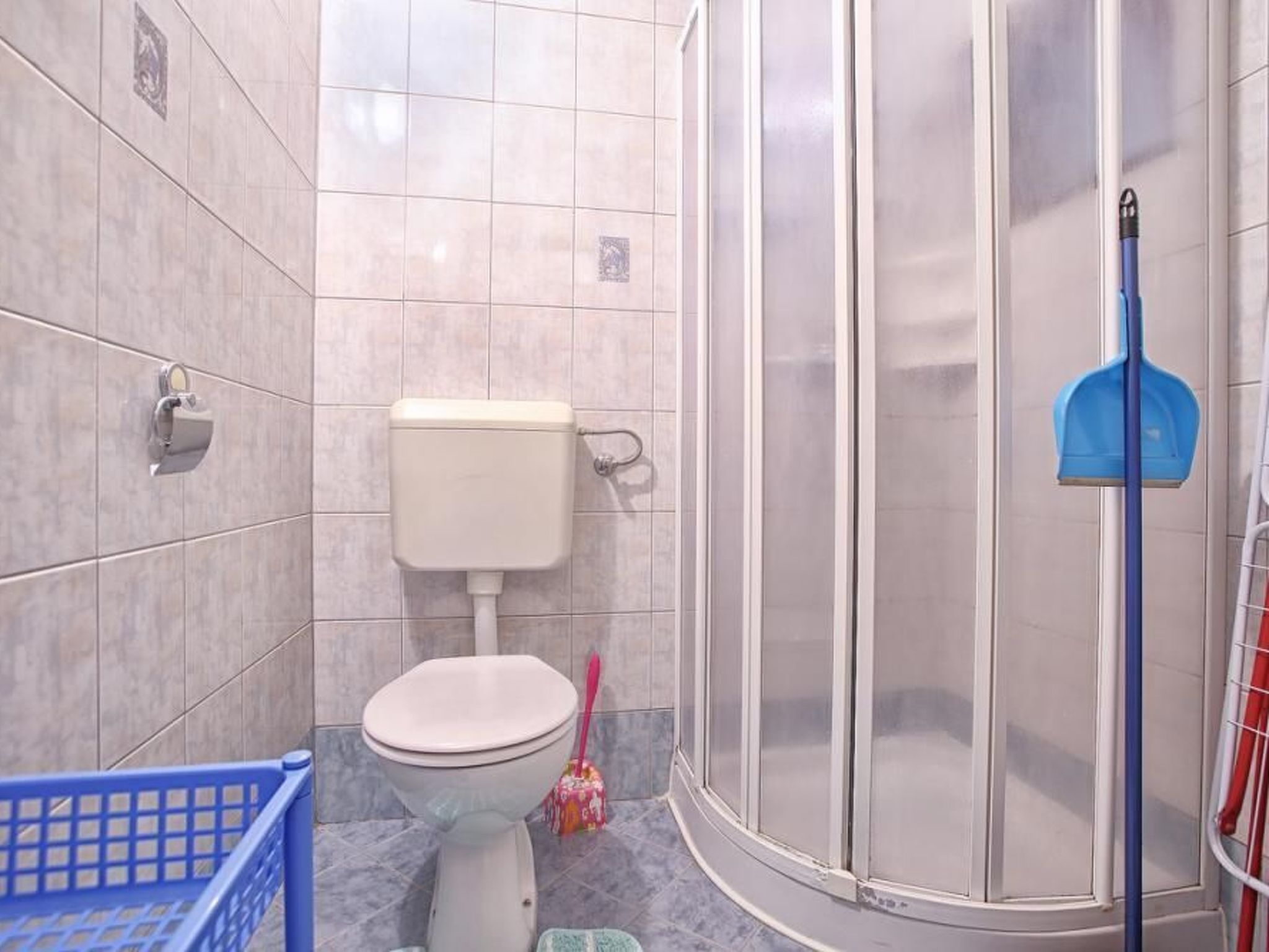 A bathroom with a toilet, shower, and a blue basket.
