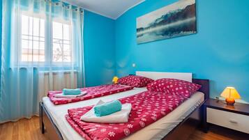 A bedroom with a large bed, two bedside lamps, a window with sheer curtains, and a painting on the wall.