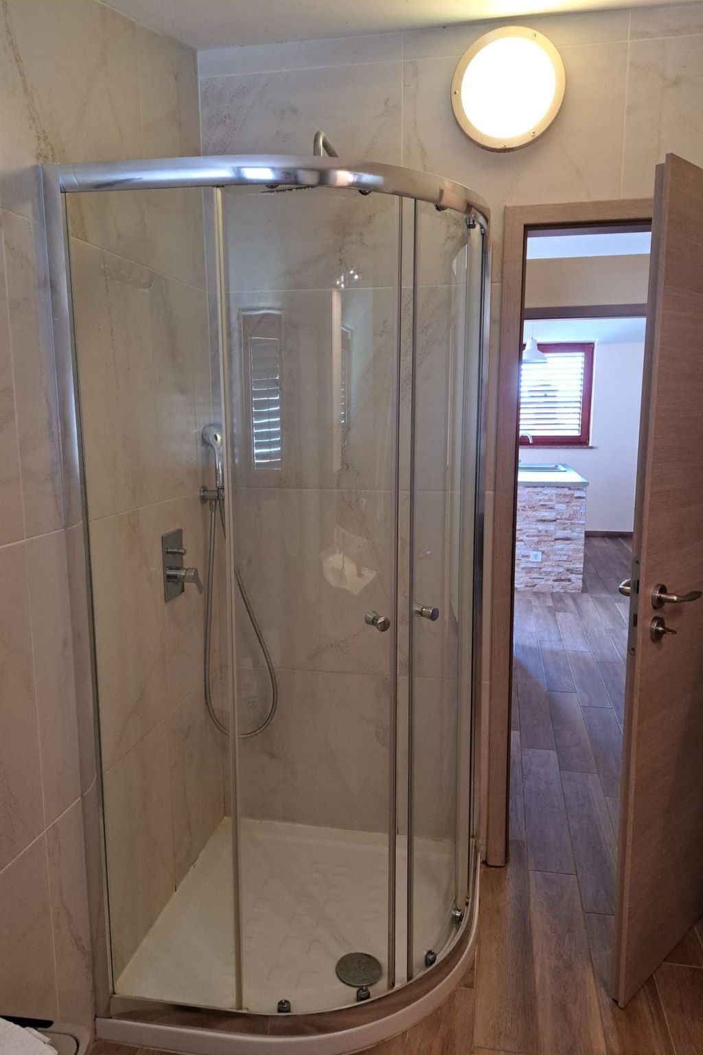 Cabina de bany amb vidre, dutxadora de mà i aixeta fixa a la paret.