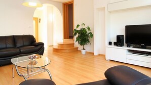 Uma sala de estar moderna com um sofá de couro preto, uma mesa de centro de vidro, uma televisão e uma planta.