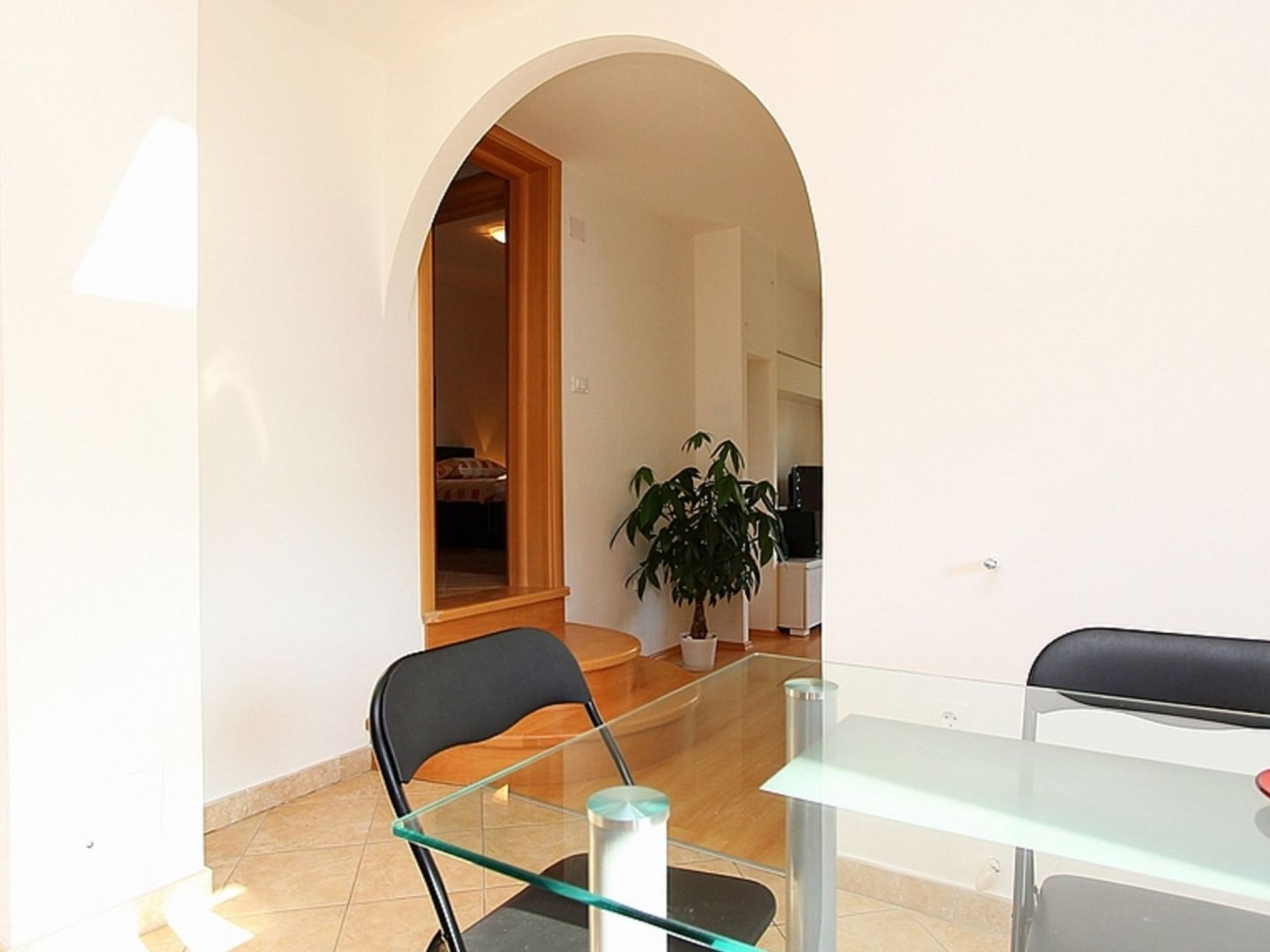 A dining area with a glass table and chairs, a potted plant, and a doorway leading to another room.