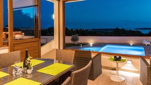 A dining area with wicker furniture and a view of a swimming pool at dusk. - Nettes Ferienhaus in Pomer mit Privatem Pool by Interhome (Medulin)