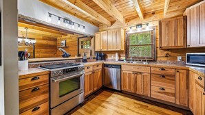Una cocina moderna con armarios de madera, electrodomésticos de acero inoxidable y un amplio ventanal con persianas.