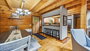 Un interior de madera con zona de comedor, cocina y taburetes de bar.