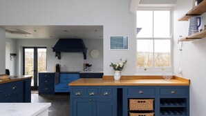 A modern kitchen with blue cabinets, a wooden countertop, and a large window. - House Annexe Sleeps 18 Heated Pool (Chichester)