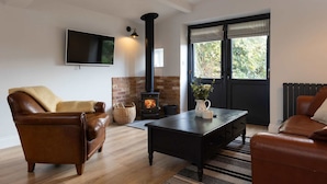 A living room with a fireplace, leather sofas, a flat-screen TV, and a large window. - House Annexe Sleeps 18 Heated Pool (Chichester)
