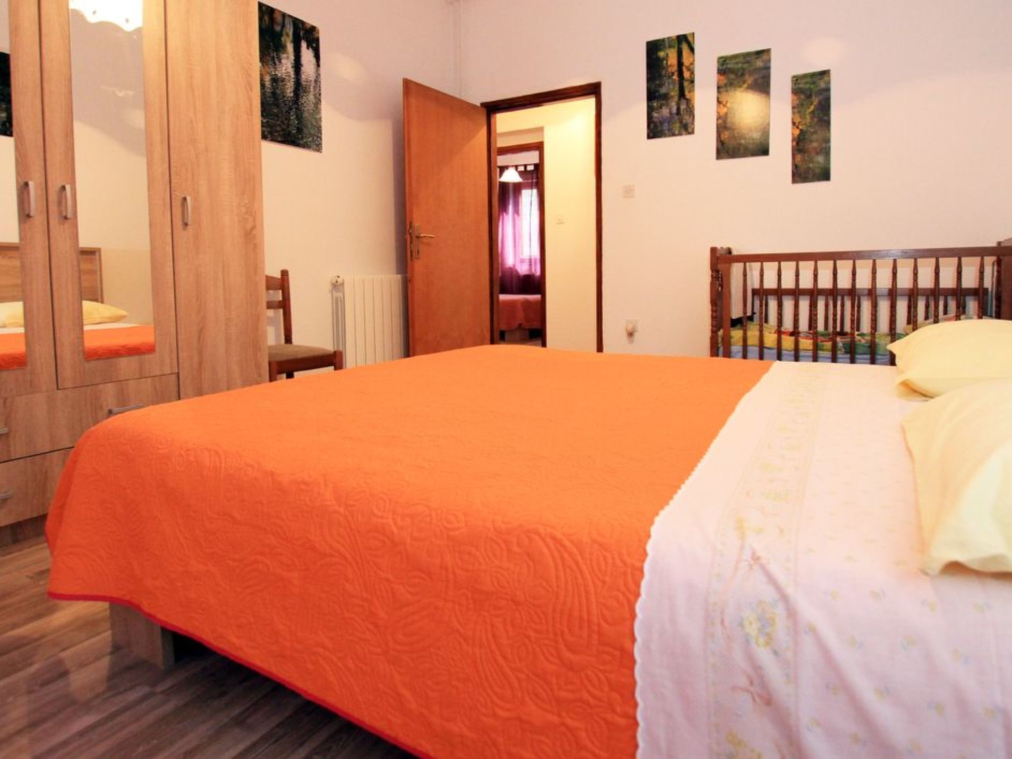 A bedroom with a large bed, wooden wardrobe, and a door leading to another room.