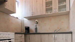 Une cuisine avec des meubles de couleur bois clair, une cuisinière blanche et un sol carrelé.