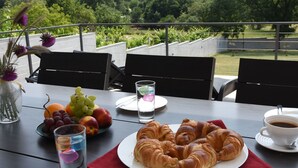 Una tavola imbandita con croissant, frutta e caffè, con vista su un giardino.