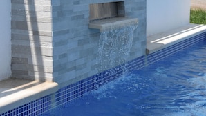 Una piscina con una parete in pietra e un piccolo elemento d'acqua.