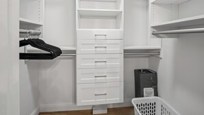 Un placard blanc avec plusieurs étagères et tiroirs, une tringle pour suspendre les vêtements et une poubelle.