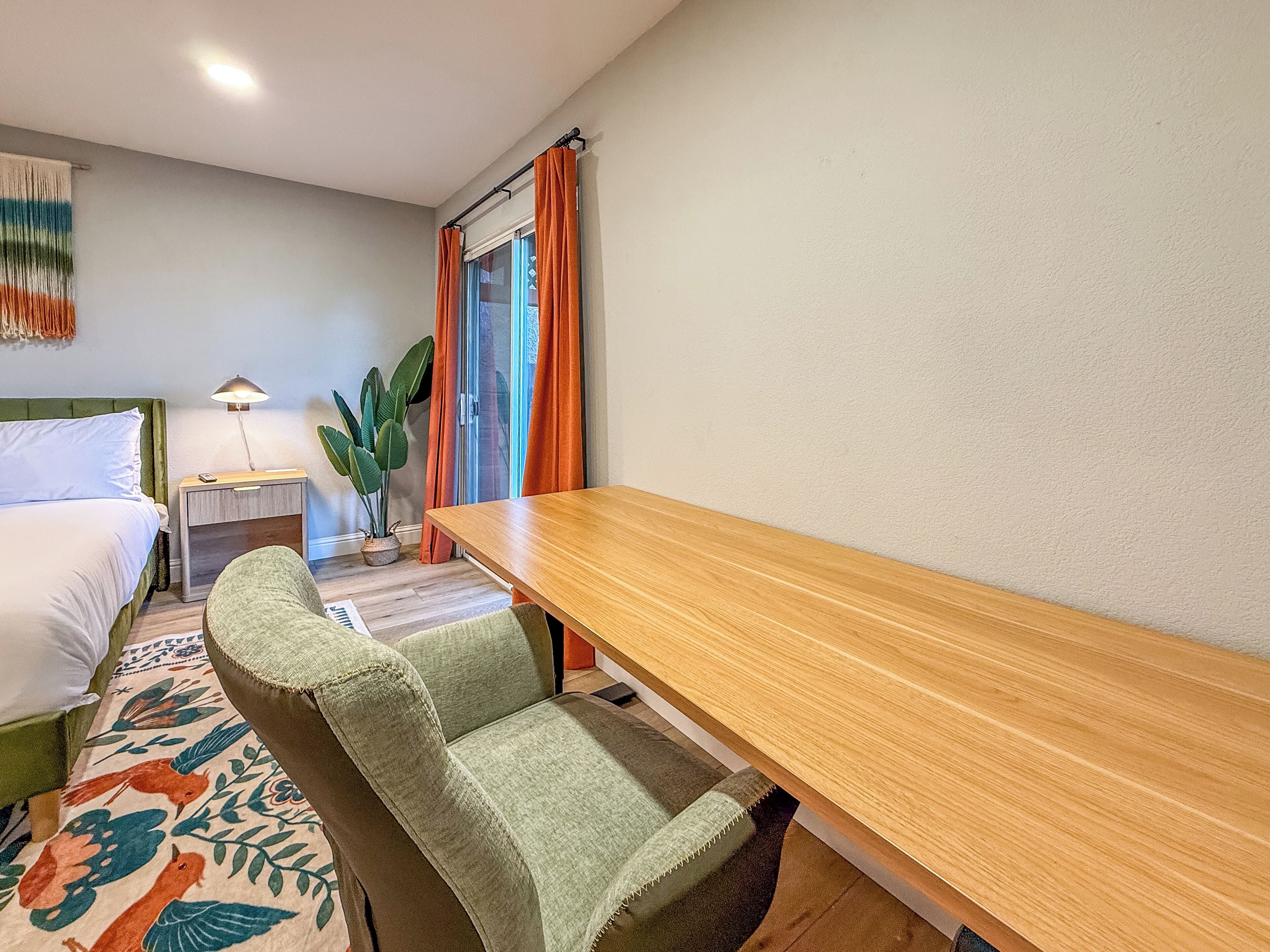 A hotel room with a bed, a desk, a chair, a lamp, and a potted plant.
