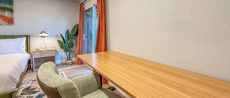 A hotel room with a bed, a desk, a chair, a lamp, and a potted plant.