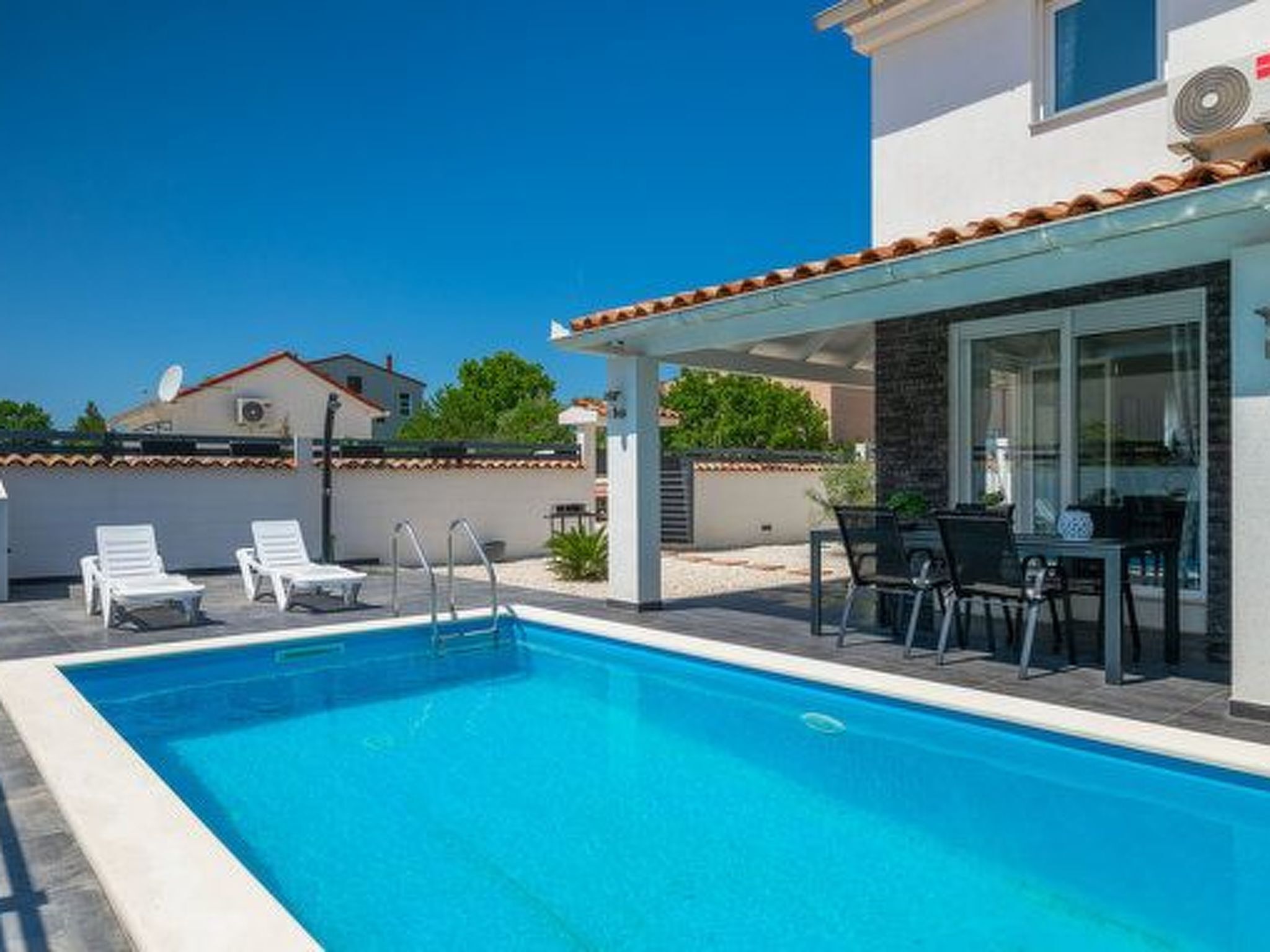 Une piscine entourée d’un patio couvert, avec des chaises longues et une table.