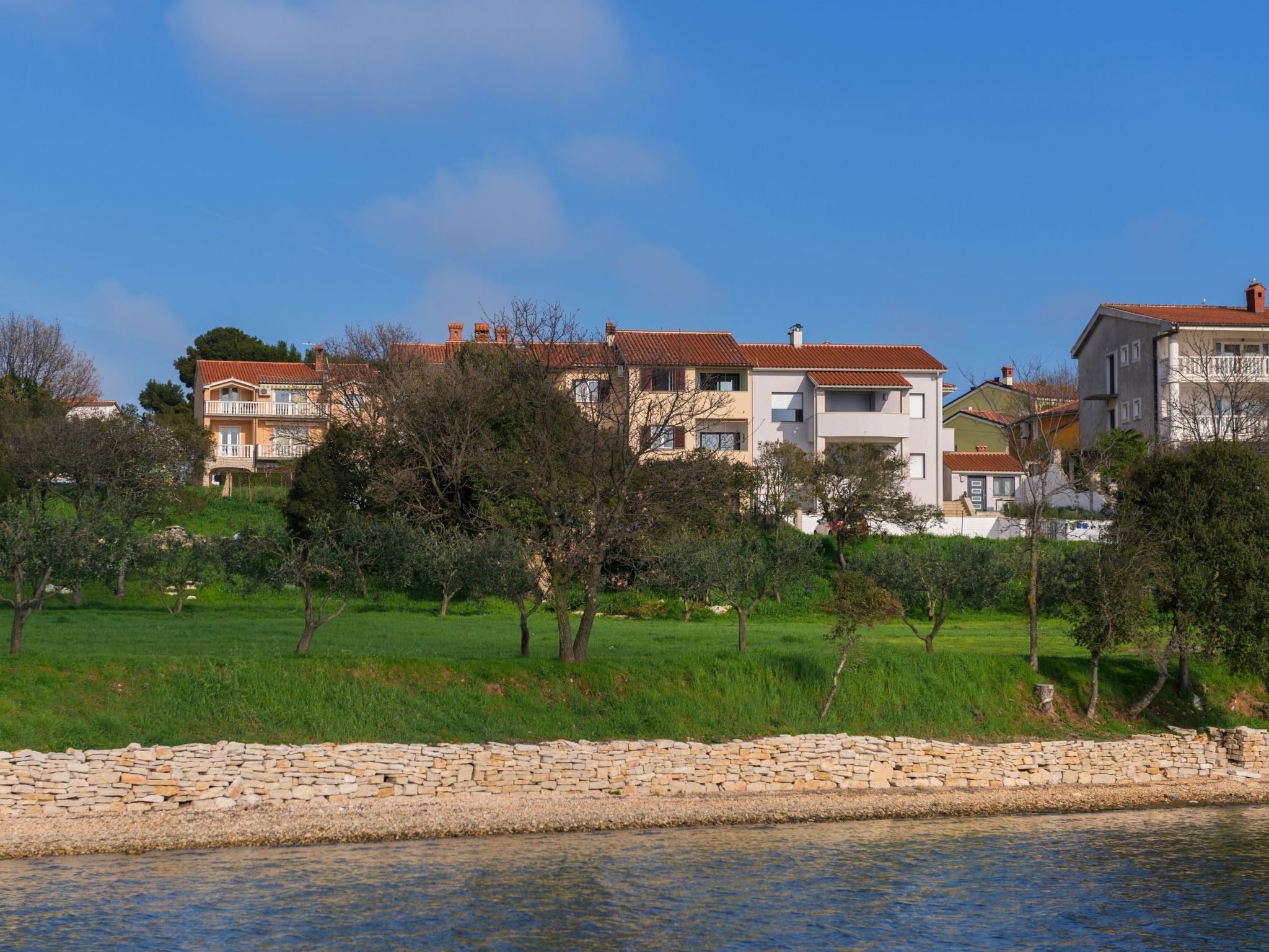 A coastal residential area with houses, a stone wall, and a body of water.