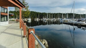 Ein Yachthafen mit vertäuten Booten, einer Holzpromenade und einem modernen Gebäude mit großen Fenstern.
