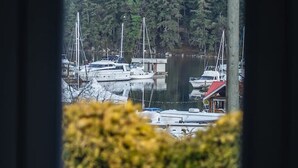 Blick durch ein Fenster auf einen Yachthafen mit mehreren Segelbooten, umgeben von dichtem Wald.