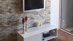 Ein modernes Wohnzimmer mit Steinwand, einem an der Wand befestigten Fernseher, einer weißen Unterhaltungsanlage und einer Glastür, die in einen anderen Raum führt.