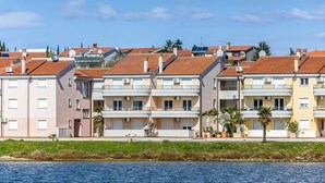 Une rangée d’immeubles à plusieurs étages dotés de balcons, un plan d’eau au premier plan et un ciel dégagé.