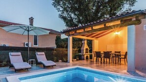 Piscina com espreguiçadeiras, área de estar coberta e churrasqueira.