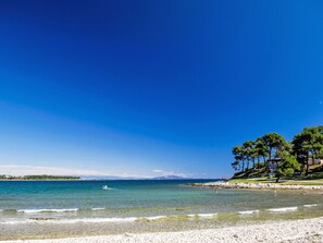 A beach with clear water, a rocky shoreline, and trees in the background. - Villa mit Garten, Grill und Terrasse by Interhome (Medulin)