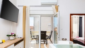 Una habitación moderna con televisión de pantalla plana, balcón con paredes de cristal, zona de comedor y zona de ducha.